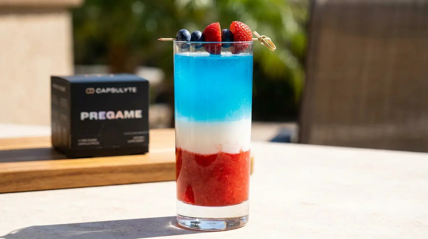 Red white and blue layered berry spritz cocktail in a tall glass with skewered strawberries and blueberries