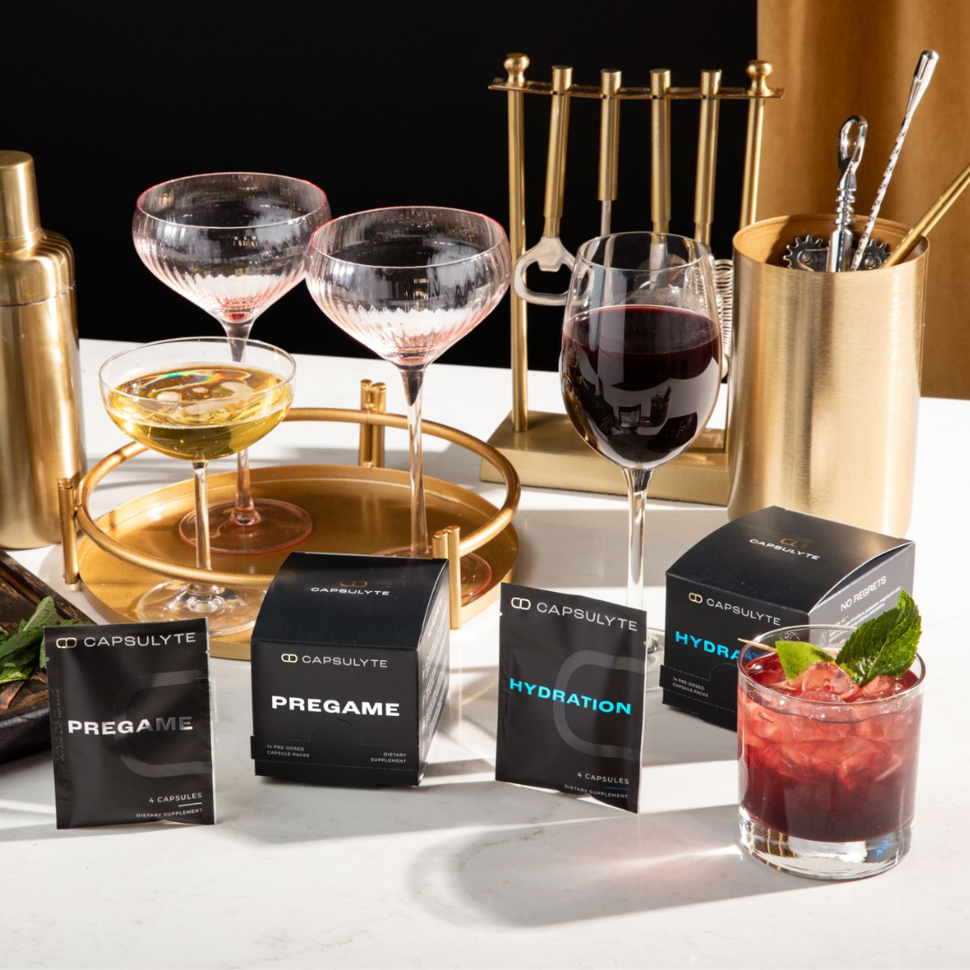 Capsulyte Pregame and Hydration dietary supplements displayed alongside cocktails and wine glasses on a bar setup. Designed for hangover prevention and hydration support, these supplements help you enjoy a night out without regrets.