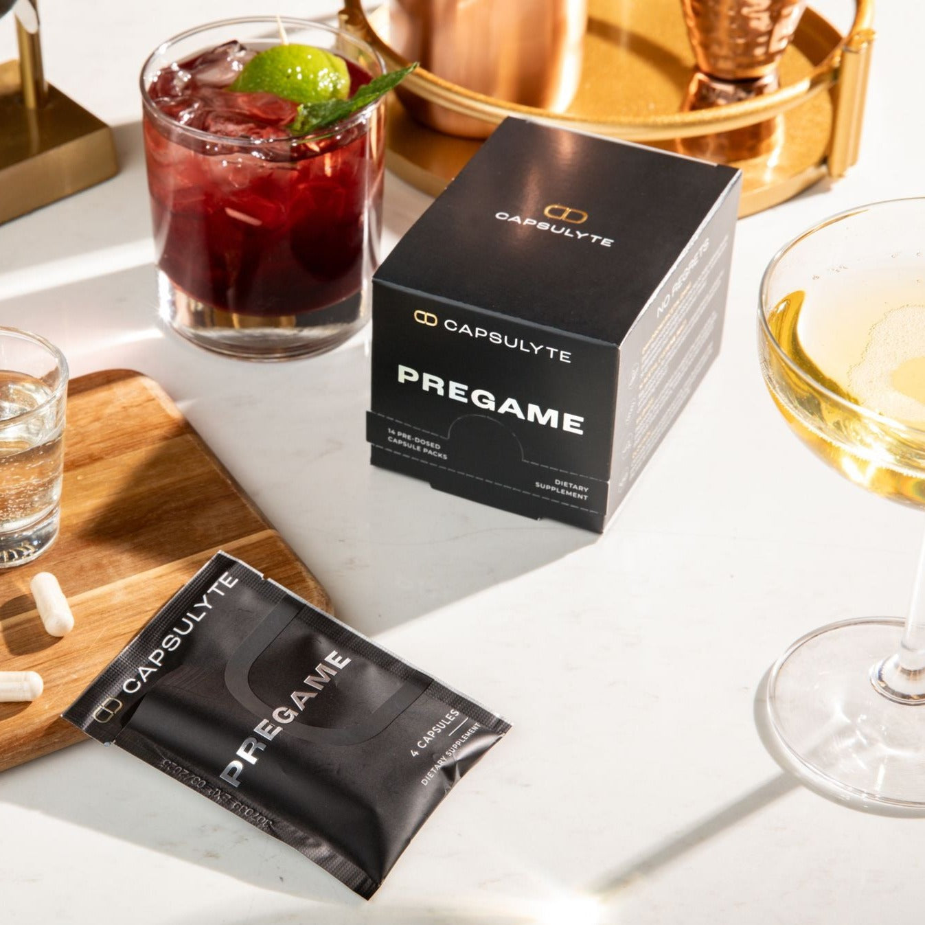 Capsulyte Pregame dietary supplement displayed on a table alongside cocktails, with a black box and a sachet containing 4 capsules. Designed to prime the body’s natural defenses, Pregame helps prevent hangover symptoms after drinking with advanced ingredients like DHM, NAC, Siliphos®, and Clovinol®