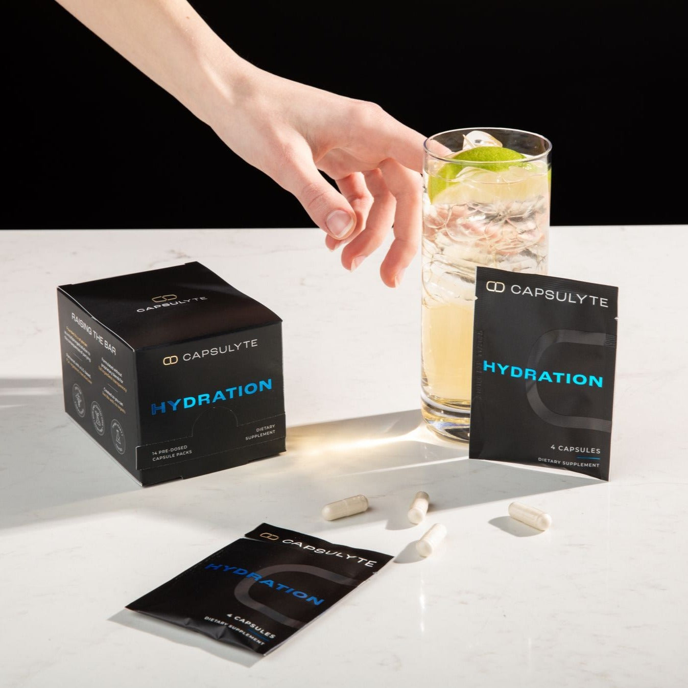 Capsulyte Hydration dietary supplement packaging displayed with a hand reaching for a refreshing cocktail, surrounded by scattered capsules. The supplement is designed for hangover prevention and maintaining hydration after drinking.